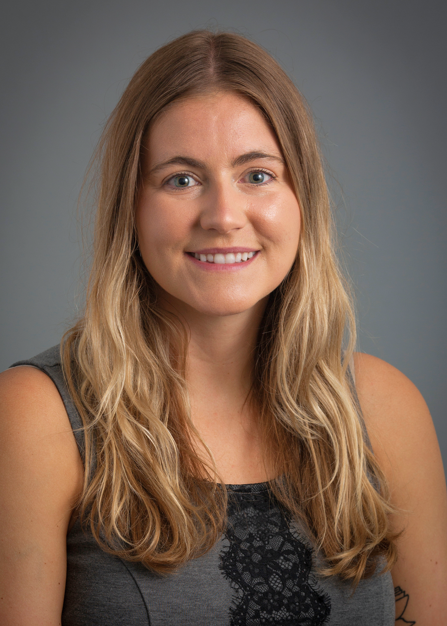 Portrait of a woman with long hair wearing a sleeveless top against a neutral gray background.