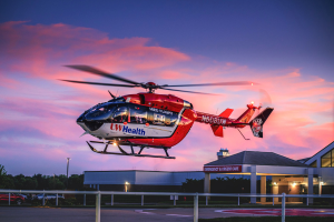 Red UW Health medical helicopter parked on a helipad at sunset, with a hospital building in the background.