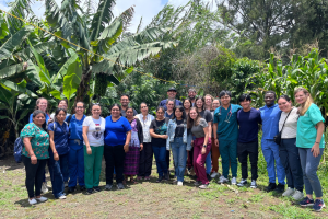 Large group of people standing together outdoors in a lush garden area with trees and greenery.