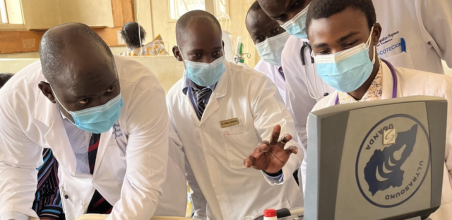 Medical professionals in white coats and masks gathered around an ultrasound machine, examining the screen.