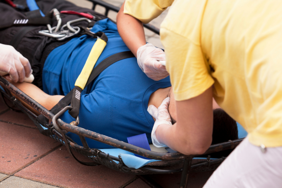 A person lays on a stretcher, with another person supporting their head and neck.