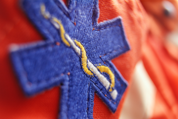 Close-up of a blue Star of Life medical emblem embroidered on bright orange fabric.