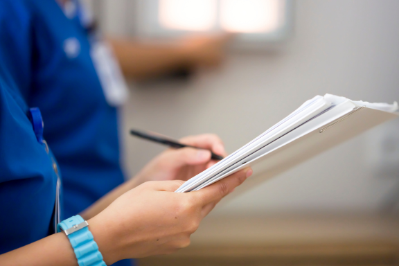 Close-up of a healthcare worker holding patient records and a pen, documenting or reviewing medical information.