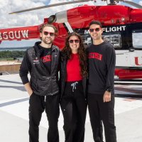 The three chief residents pose in front of a Med Flight helicopter wearing sunglasses and black and red University of Wisconsin clothing.