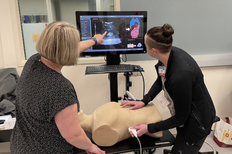 A resident practices abdominal ultrasound on a simulation manikin, with faculty instruction.